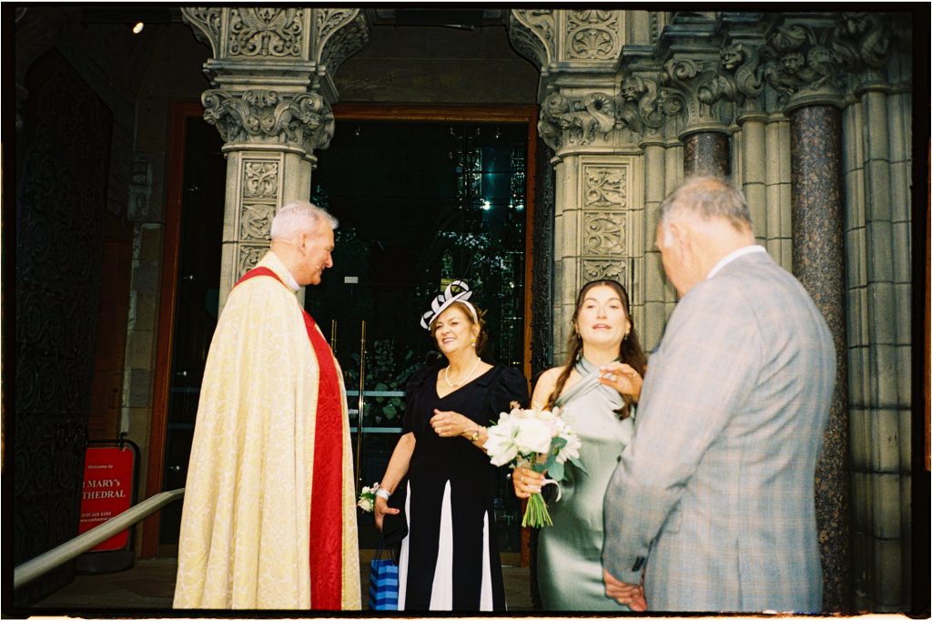 analogue photo of minister, man in a grey suit, talking to two women outside a wedding ceremony at St Mary's Episcopal Church in Edinburgh taken on 35mm film