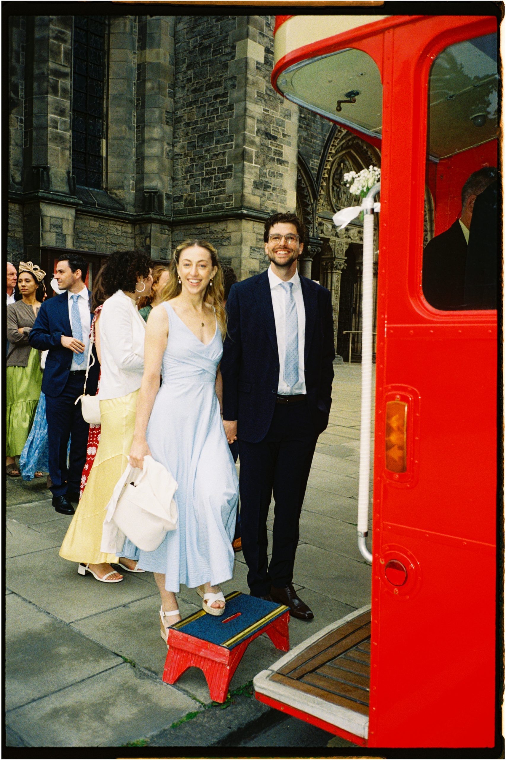 wedding guests boarding a red bus outside St Mary's Episcopal Church in Edinburgh on analogue film