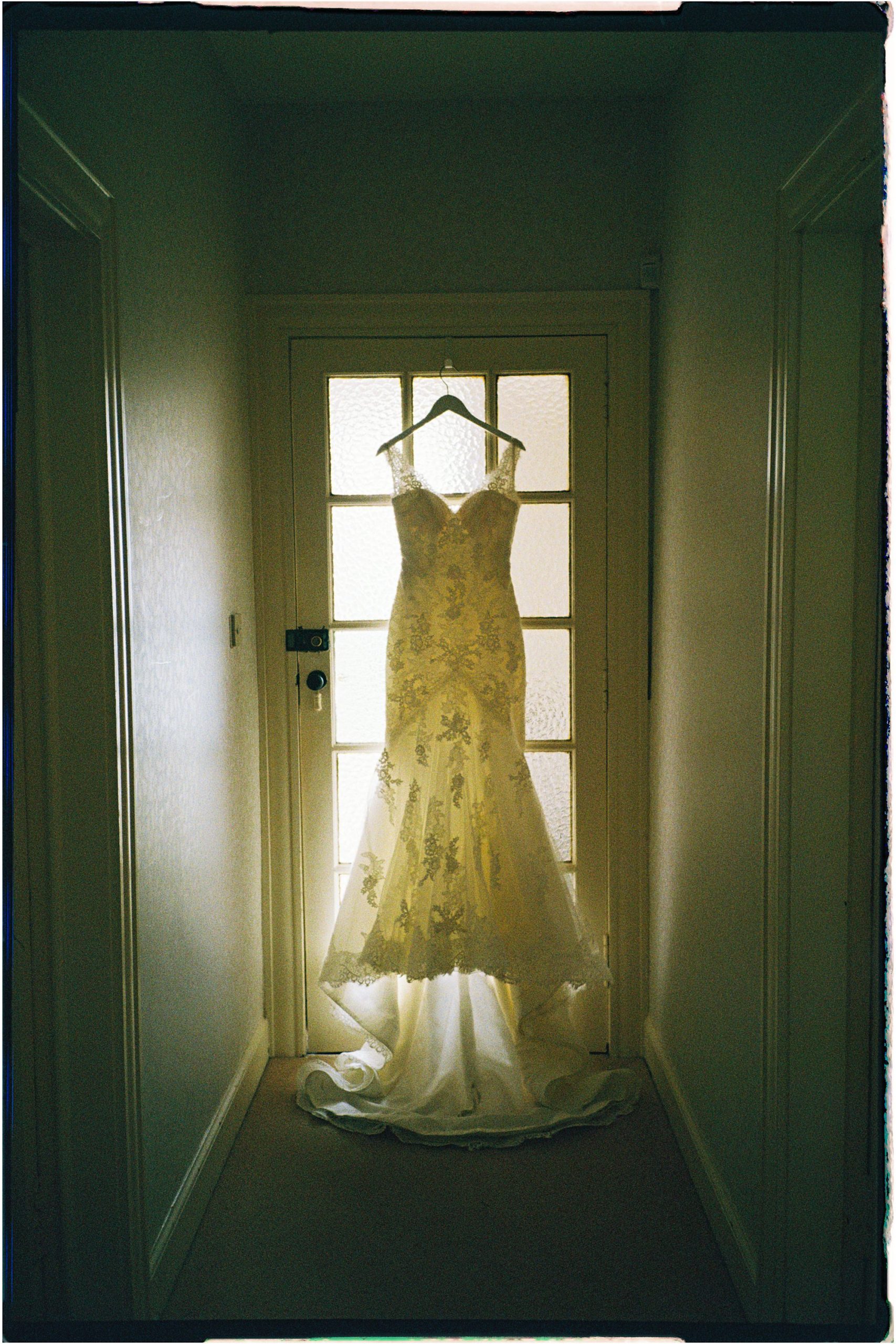 wedding dress hanging on a glass door, in a corridor, taken on 35mm film