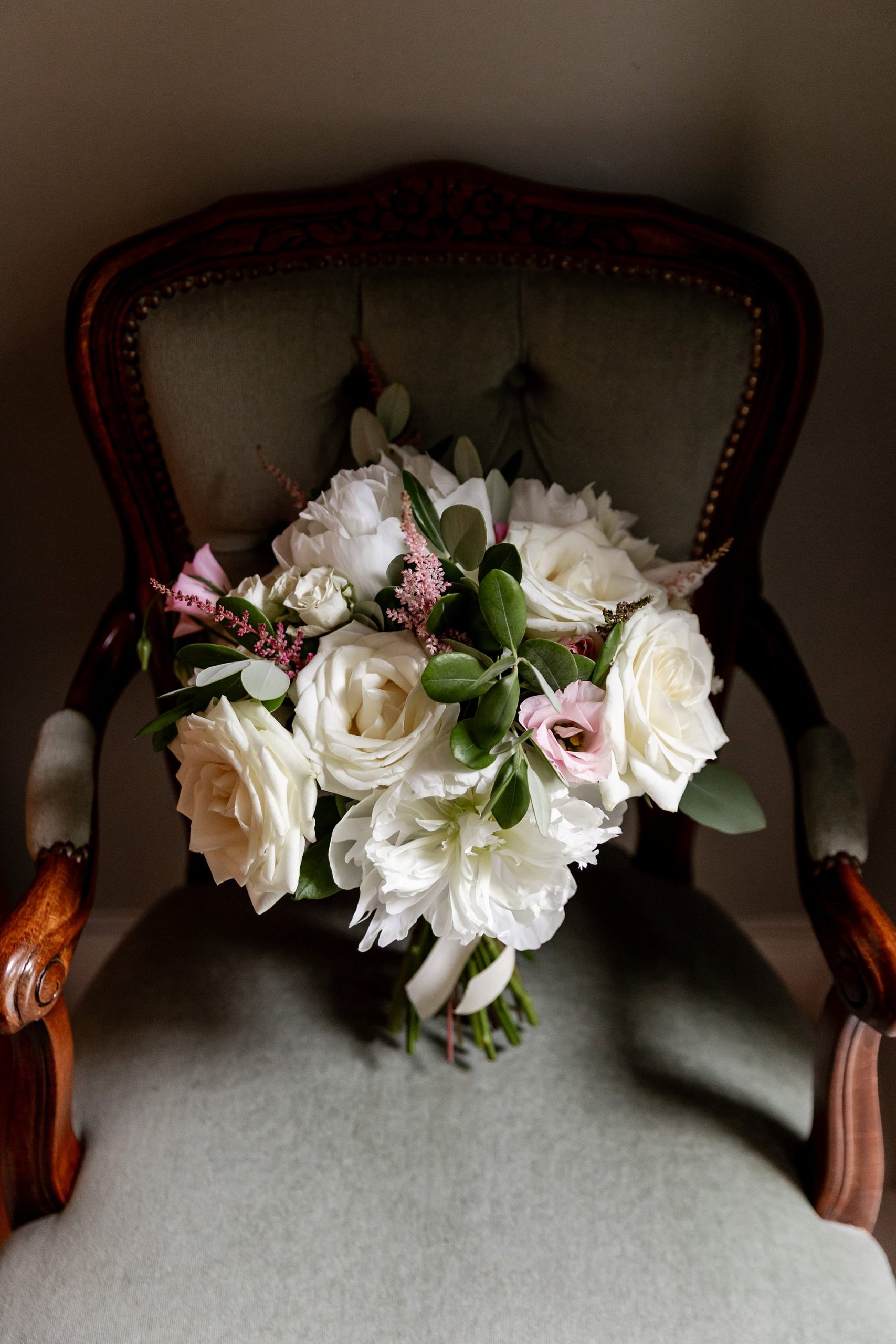 bridal bouquet of wedding flowers by Garland Florist, standing on a fabric cushioned wooden chair.
