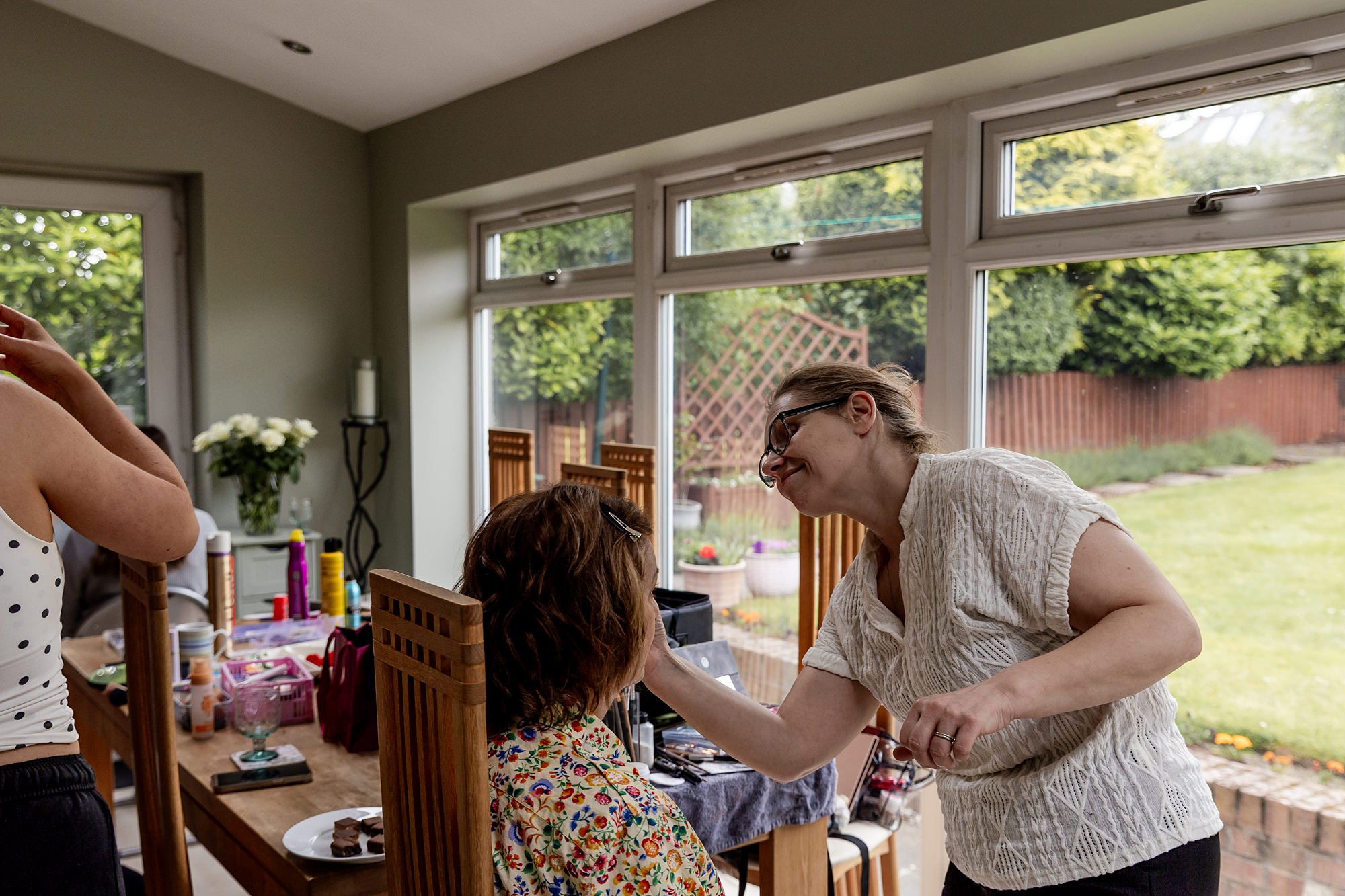 photo of HMUA applying make up to a client, in a bright room with large windows